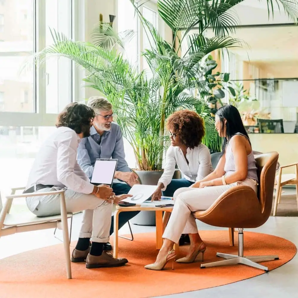 A group of four colleagues sit at a small round table having a discussion.