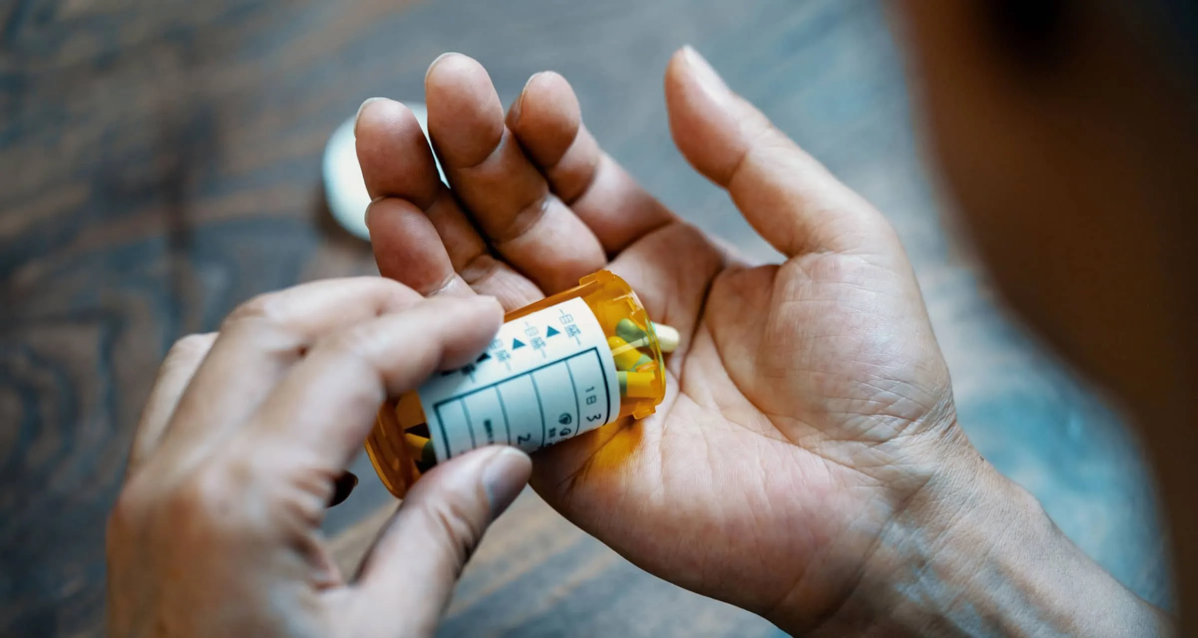 Close-up of a male hand holding a pill bottle pouring medication into his hand.